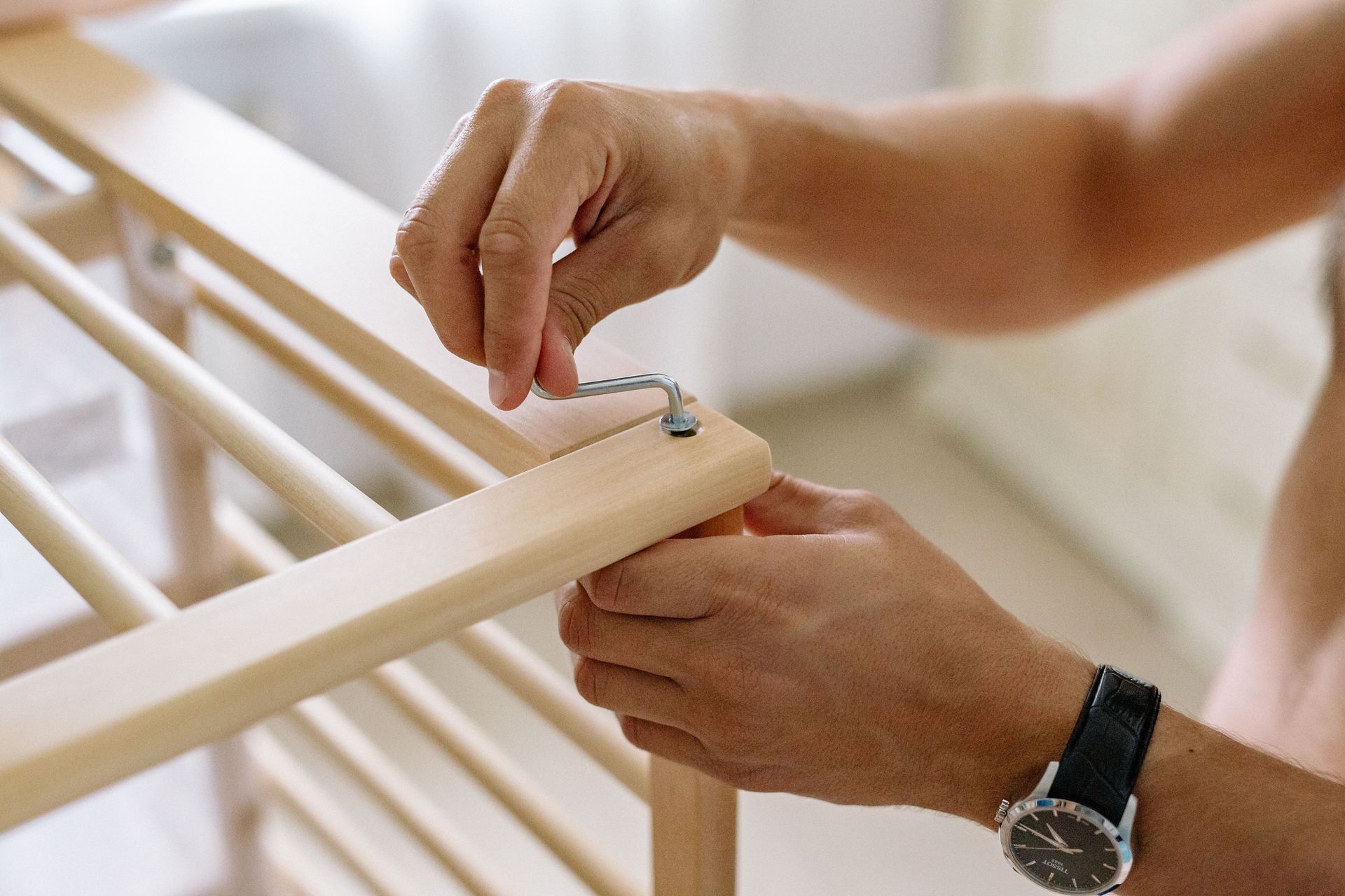Close-up of a man using an Allen wrench to assemble a wooden baby cot indoors.
